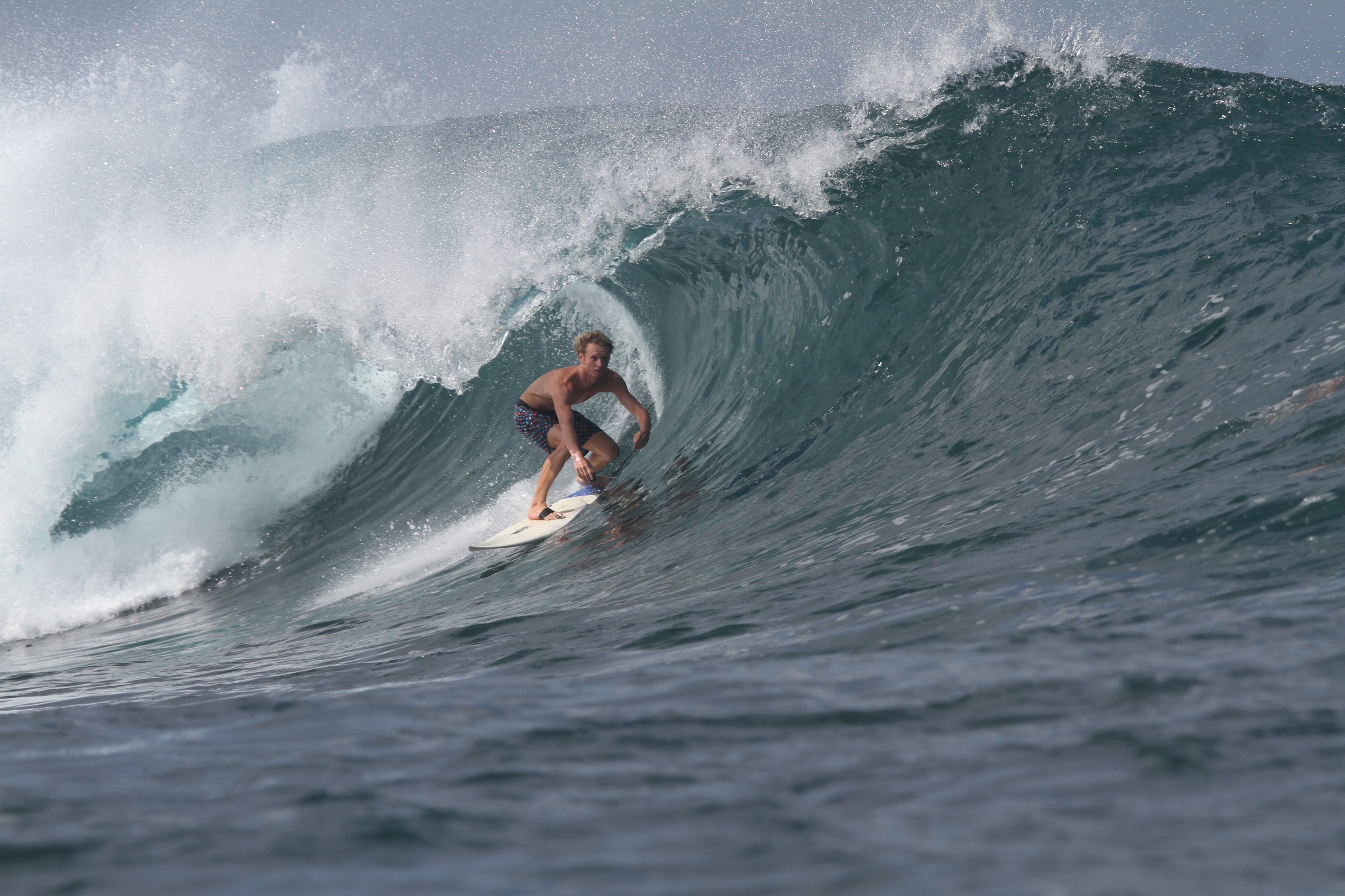 Surfer crouching in the barrel of a large grey-green wave out in open water
