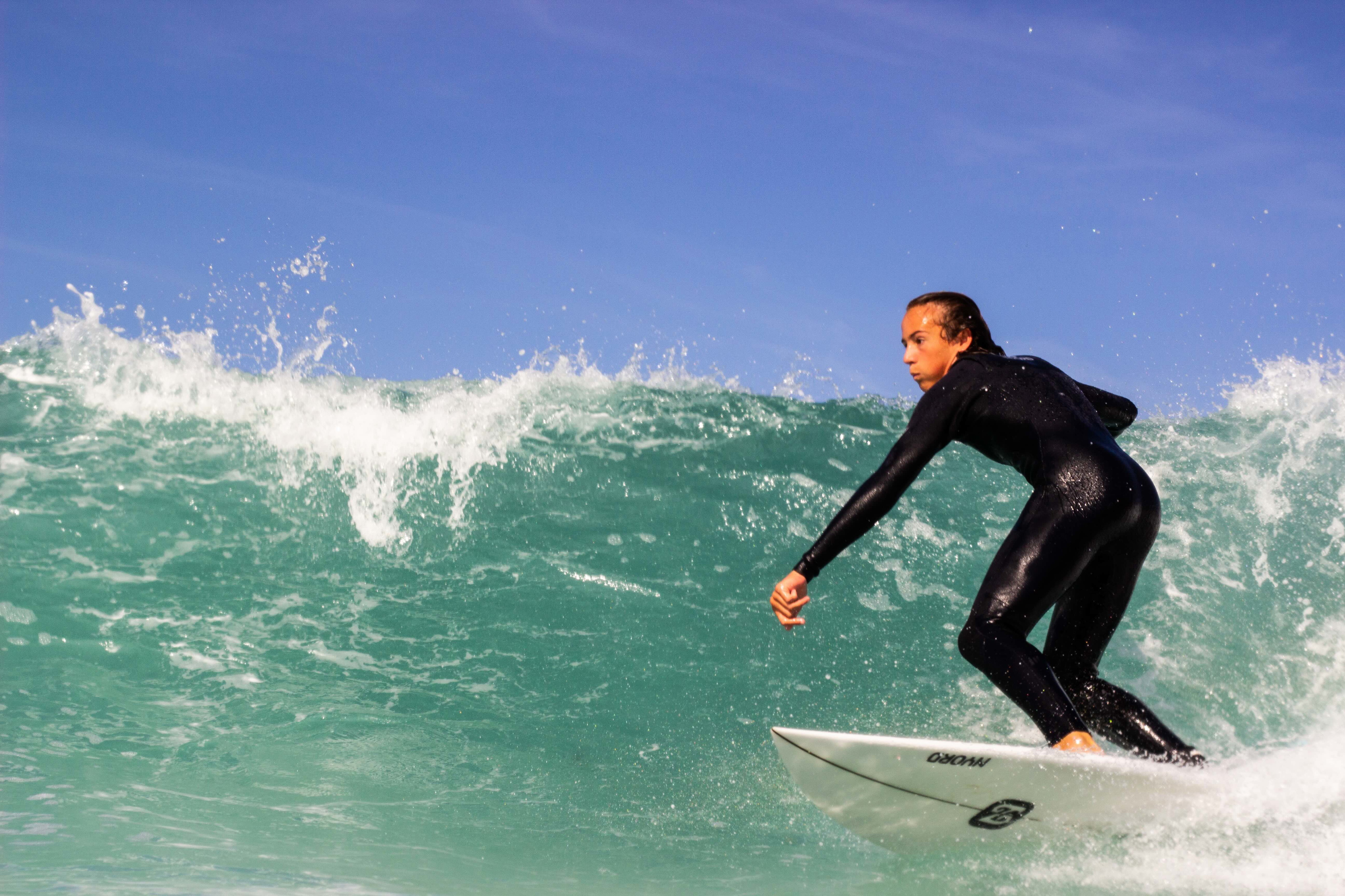 Surfer in a black wetsuit riding the face of a clean green wave on a white board