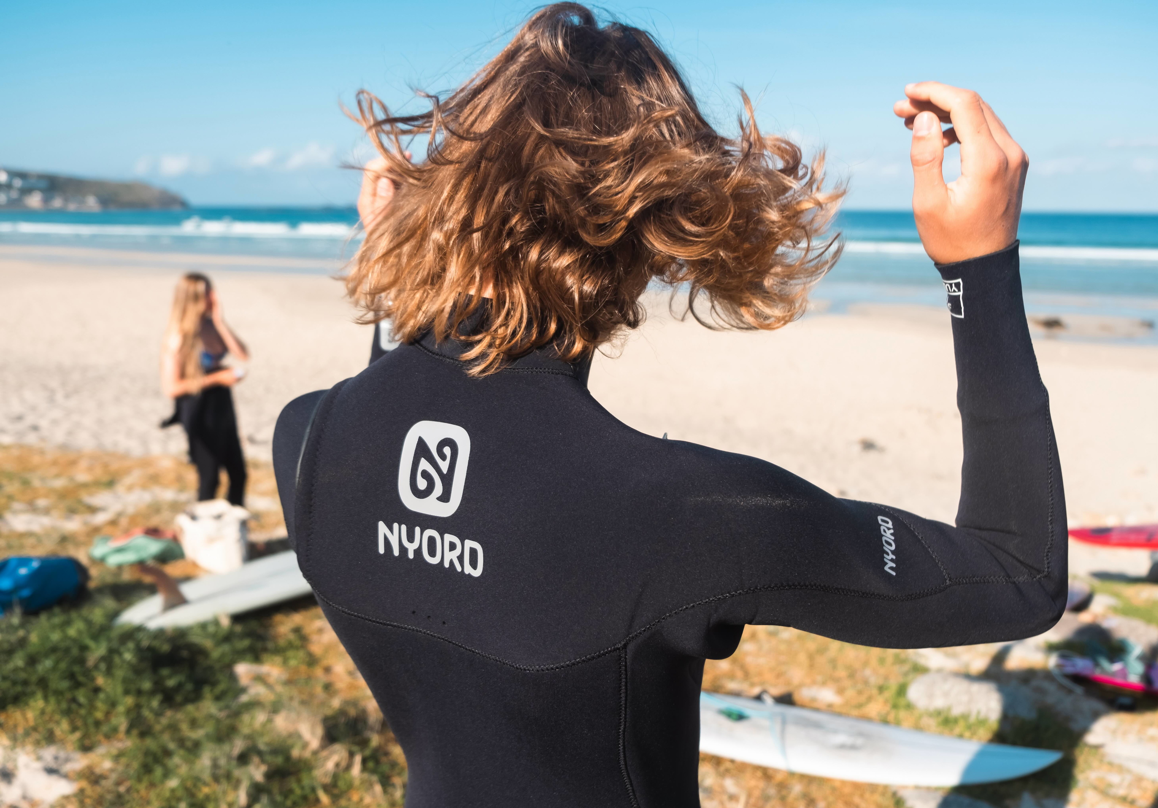 Surfer seen from behind on a sunny beach shaking out wet hair in a black Nyord wetsuit