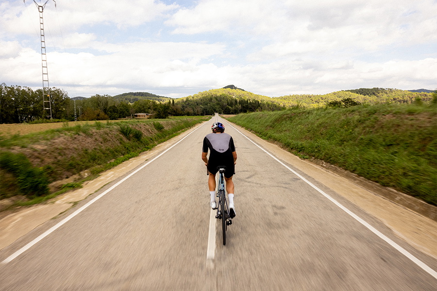 Cyclist riding away down an empty country road between green fields