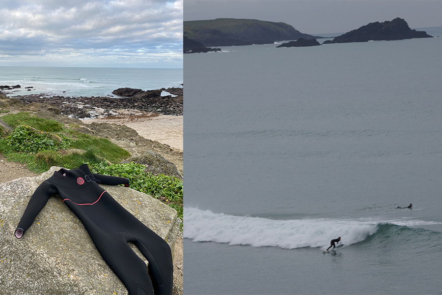 A black wetsuit laid out to dry on a coastal rock beside a surfer riding a wave
